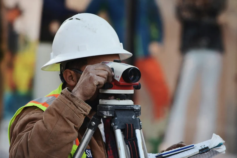 Surveyor in hard hat using a theodolite to measure a construction site