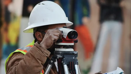 Surveyor in hard hat using a theodolite to measure a construction site
