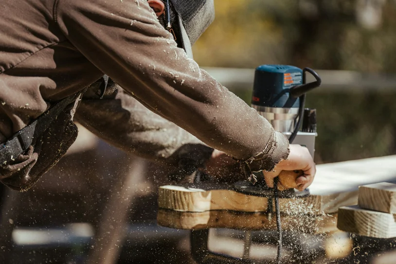 Carpenter cutting a wood plank with a power saw, sawdust flying