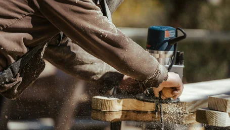 Carpenter cutting a wood plank with a power saw, sawdust flying