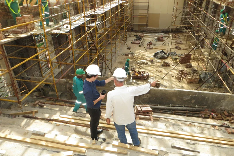 Construction site supervisors reviewing scaffolding and rebar work with a worker on site