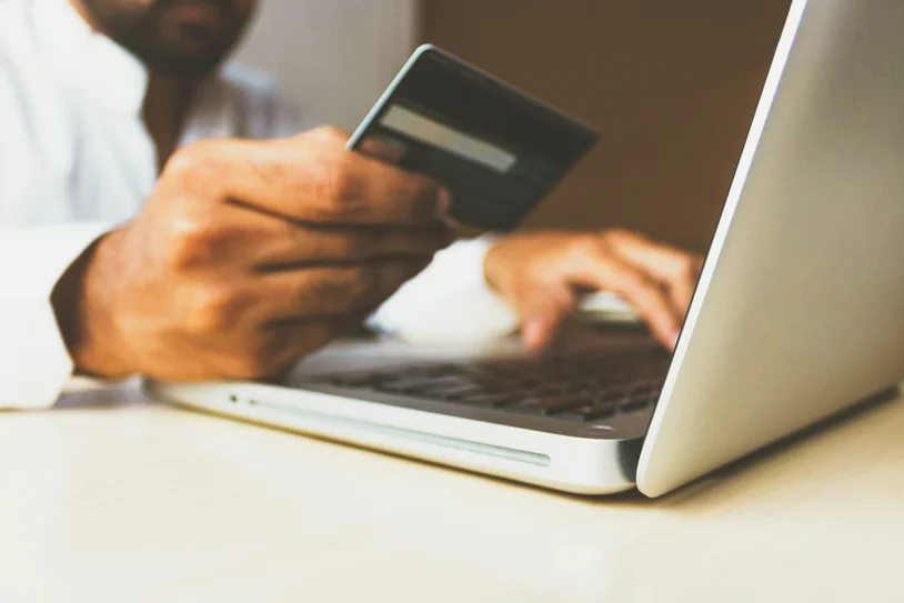 Close-up of hands holding a credit card while typing on a laptop keyboard