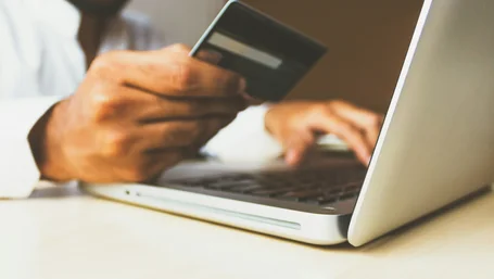 Close-up of hands holding a credit card while typing on a laptop keyboard