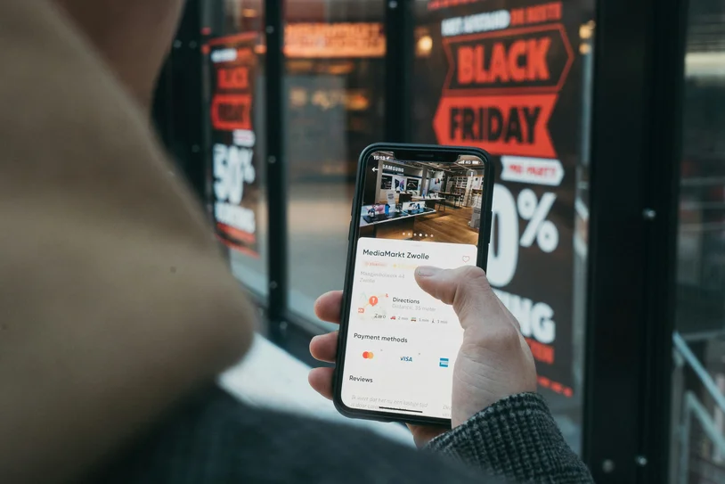 Hand holding a smartphone showing a payment app in front of a Black Friday store display