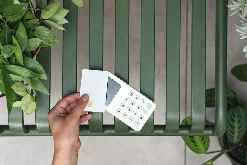 Hand holding a card payment terminal above a green outdoor bench