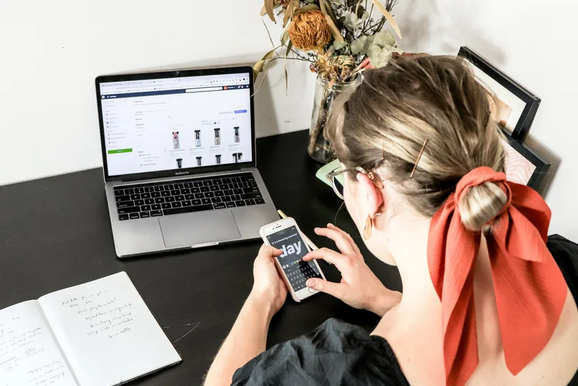 Woman viewed from above using a smartphone next to an open laptop with a product dashboard