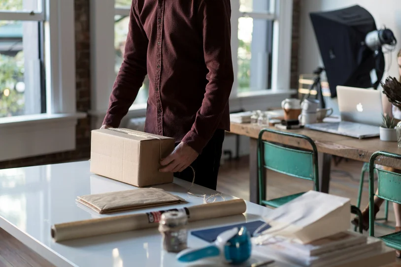 Person packing a cardboard box on a desk in a bright home office