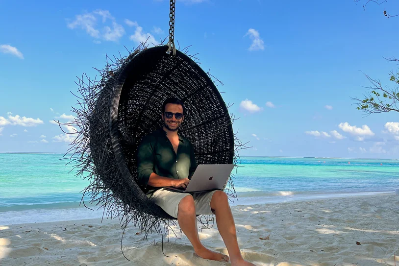 Person working on a laptop while sitting in a beach swing chair by the ocean