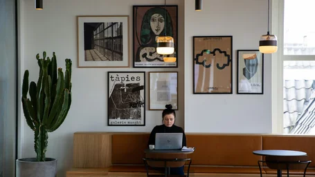 Person working on a laptop at a small table surrounded by framed art prints