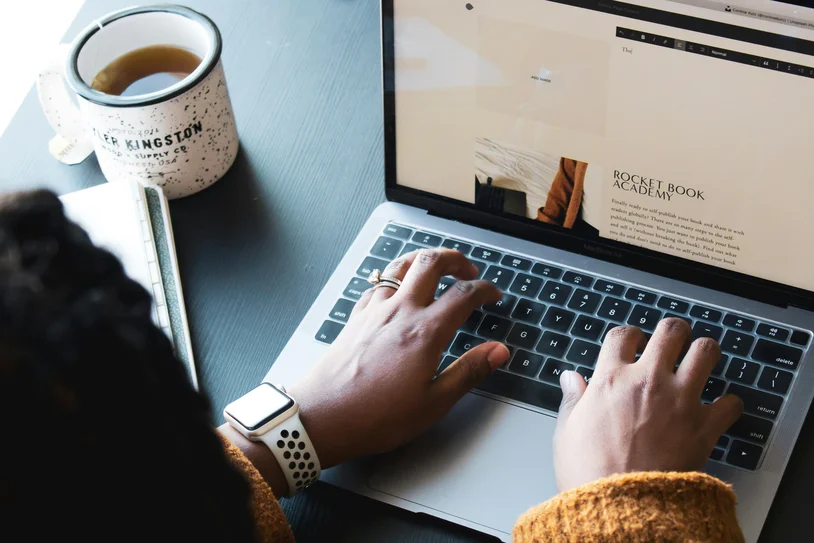 Close-up of hands typing on a laptop with a mug of tea nearby