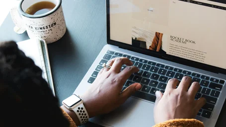 Close-up of hands typing on a laptop with a mug of tea nearby