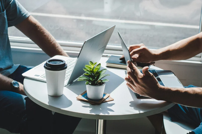 Two people working together at a small table with coffee and a plant