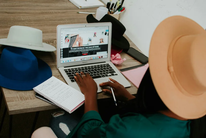 Person browsing a shopping website on a laptop with sun hats nearby