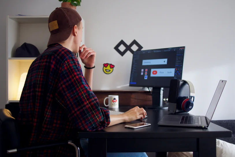 Person wearing headphones working at a home desk setup with dual monitor and laptop