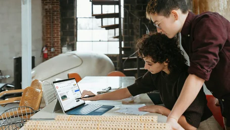Two people collaborating while looking at a laptop screen together