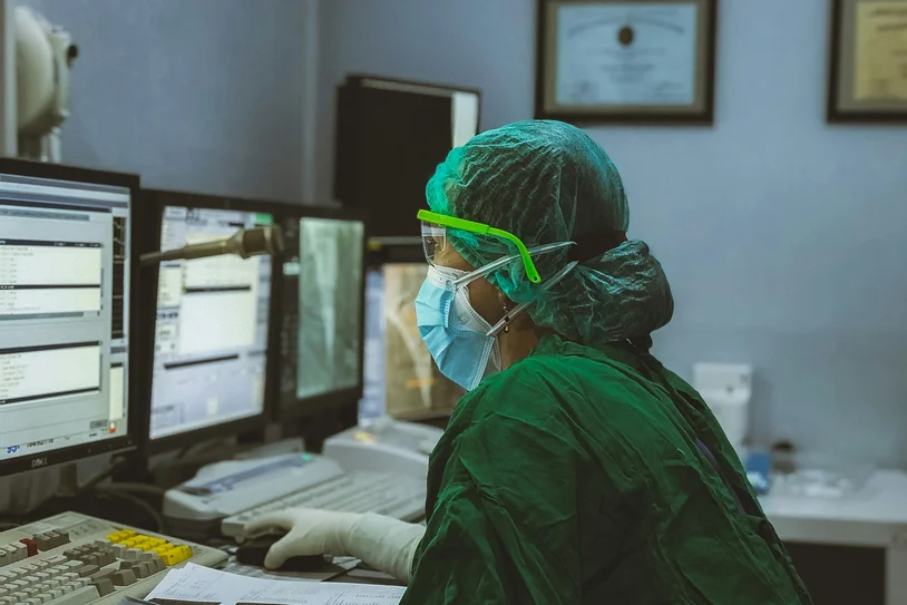 Surgeon in scrubs reviewing patient records on multiple monitors