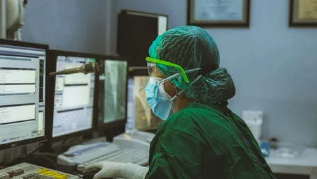 Surgeon in scrubs reviewing patient records on multiple monitors