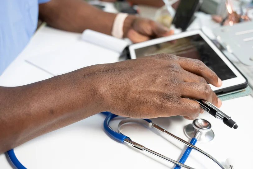 Close-up of a provider's hand resting on a tablet next to a stethoscope on a desk