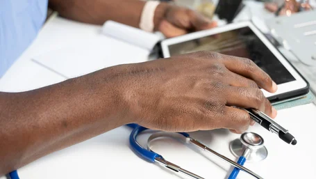 Close-up of a provider's hand resting on a tablet next to a stethoscope on a desk