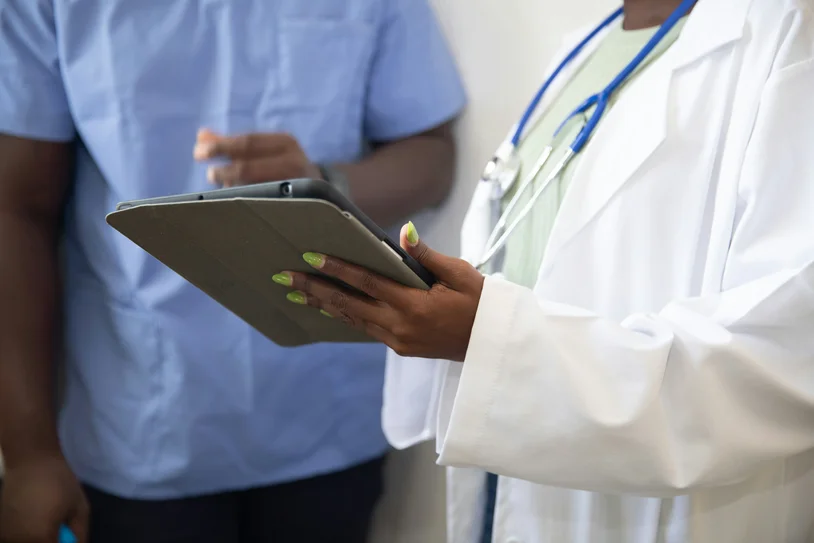 Close-up of a provider's hand holding a tablet beside a colleague in scrubs