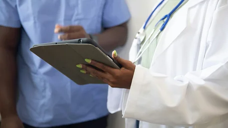Close-up of a provider's hand holding a tablet beside a colleague in scrubs