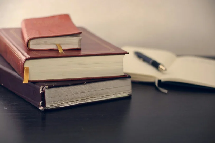 Stack of leather-bound legal books beside an open notebook and pen