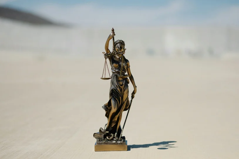 Small bronze Lady Justice statue standing outdoors against a bright sky