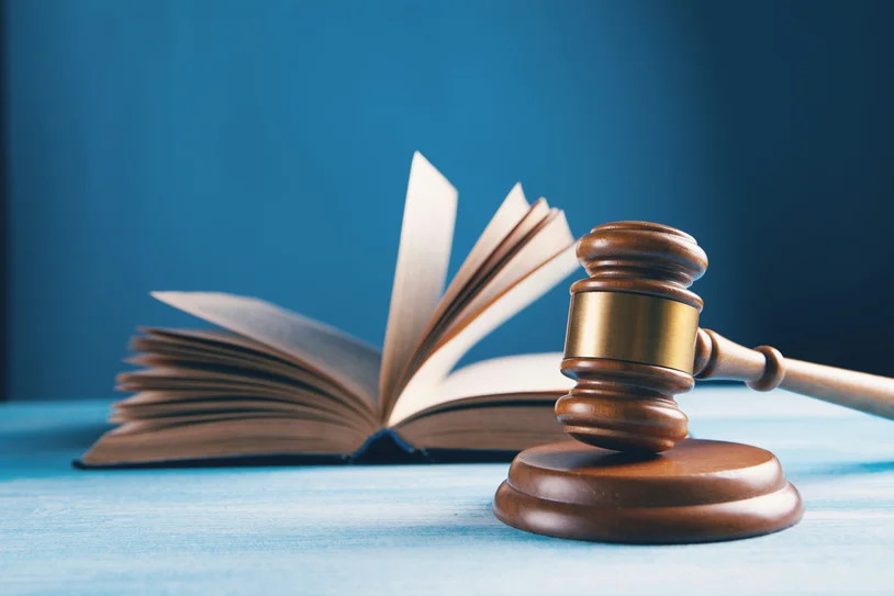 Wooden judge's gavel beside an open law book on a blue desk