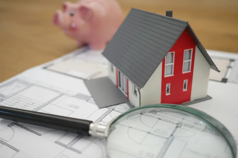 Miniature house model with a piggy bank and magnifying glass on house blueprints