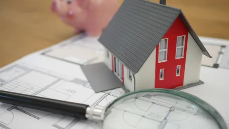Miniature house model with a piggy bank and magnifying glass on house blueprints