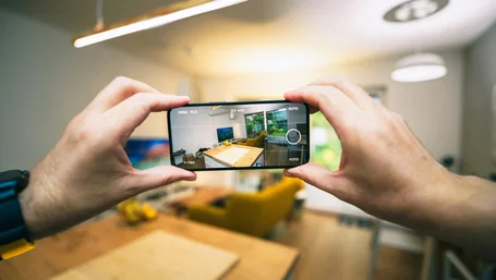 Close-up of hands photographing a bright living room with a smartphone