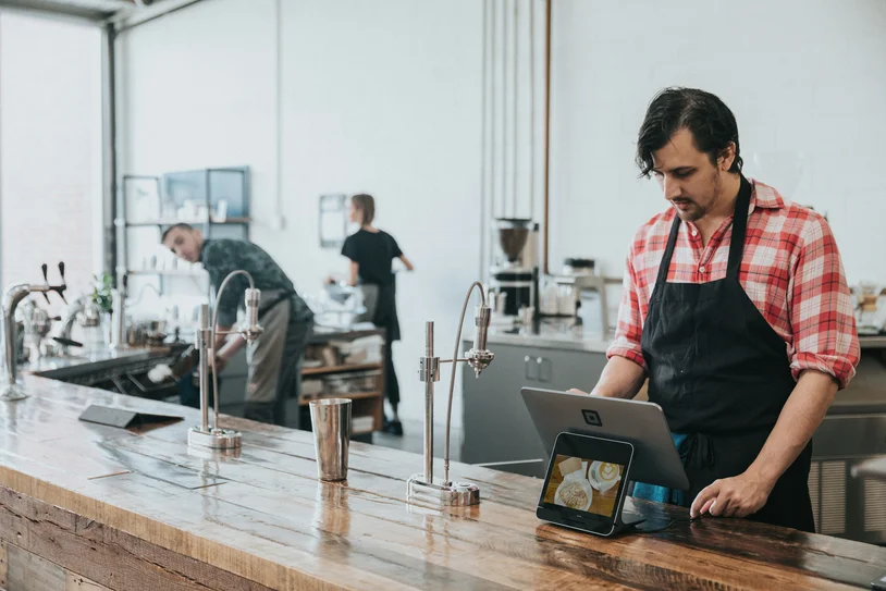 Barista using a point-of-sale tablet behind a wooden counter