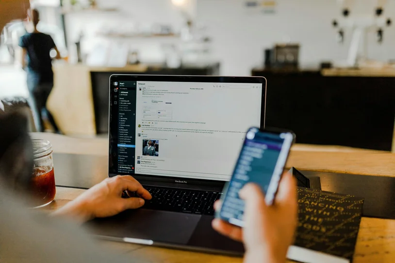 Hands using a laptop and smartphone together at a café table
