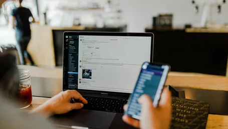 Hands using a laptop and smartphone together at a café table
