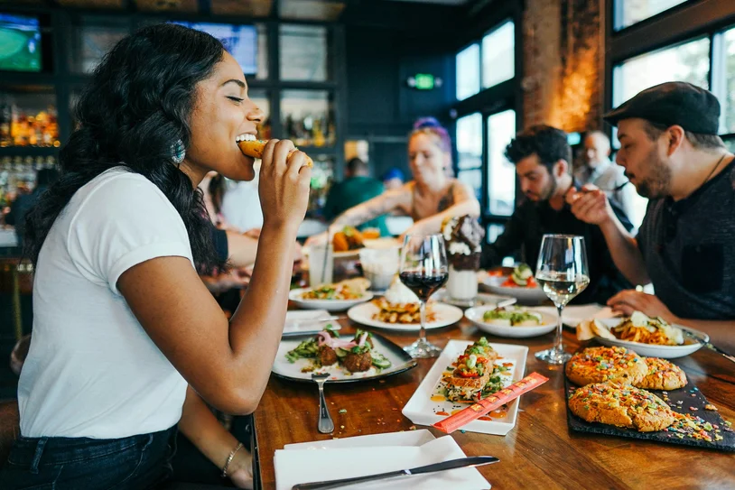 Woman happily eating at a busy restaurant table filled with shared plates