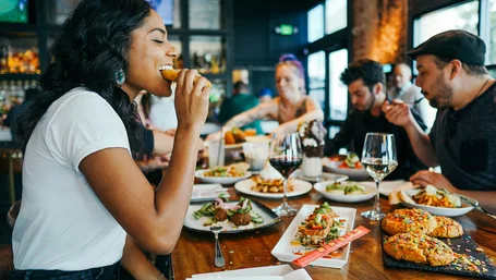 Woman happily eating at a busy restaurant table filled with shared plates