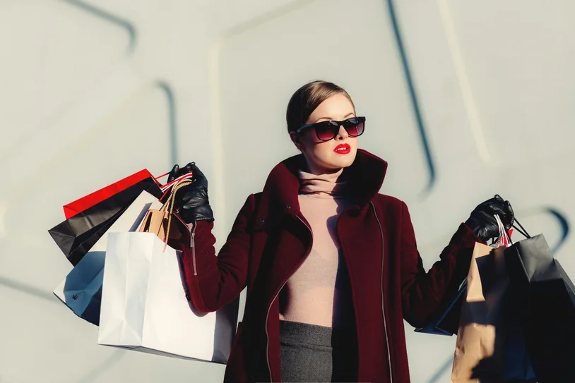 Woman in red coat holding several shopping bags in bright daylight