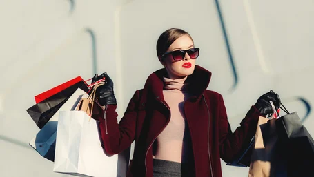 Woman in red coat holding several shopping bags in bright daylight